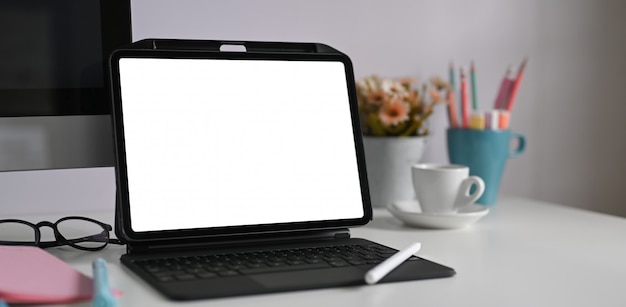 Una tableta de computadora con una funda de teclado se coloca en un escritorio blanco rodeado de varios equipos