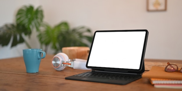 La tableta de la computadora de la pantalla en blanco con una funda del teclado está poniendo en un escritorio de madera.