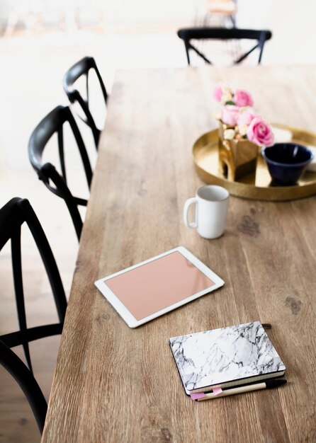 Tableta digital y un cuaderno de textura de mármol en una mesa de comedor de madera