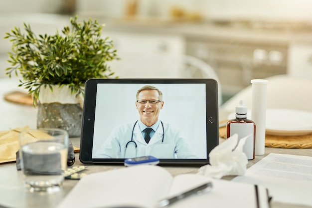 Tableta digital con una imagen de un médico apoyado sobre una mesa llena de medicación