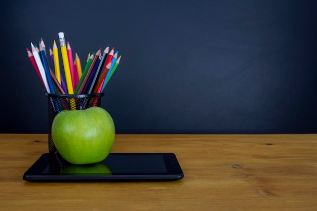 Tableta digital y manzana en el escritorio frente a la pizarra