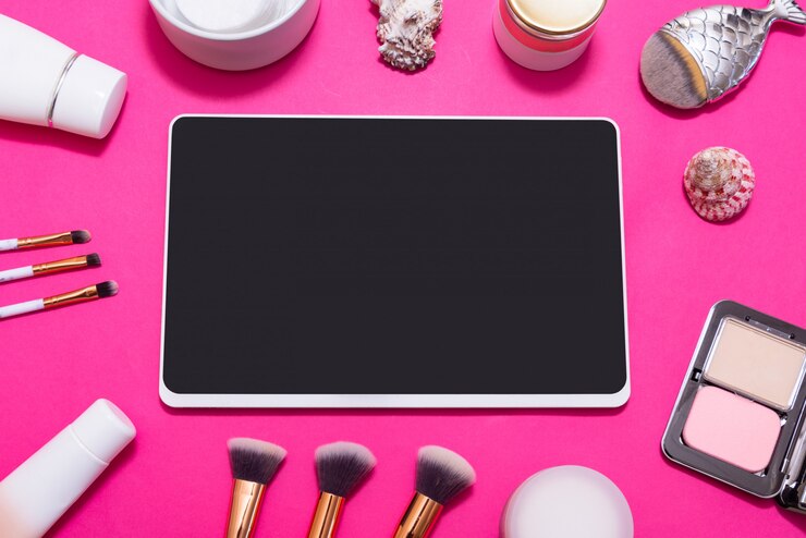 Foto tableta digital y mucho maquillaje en mesa rosa, vista superior, flatlay
