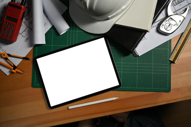Tableta digital plana con casco de pantalla en blanco y plano en la estación de trabajo del ingeniero