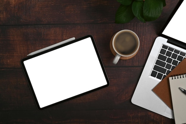 Tableta digital plana, portátil, taza de café, portátil y planta en maceta en el escritorio de la oficina de madera Pantalla blanca para el texto publicitario