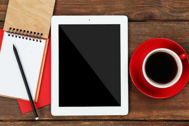 Tableta digital con una taza de café y un cuaderno en la mesa de madera, primer plano