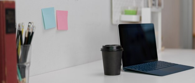 Tableta digital con teclado inalámbrico, vaso de papel y papelería en mesa de trabajo moderna blanca