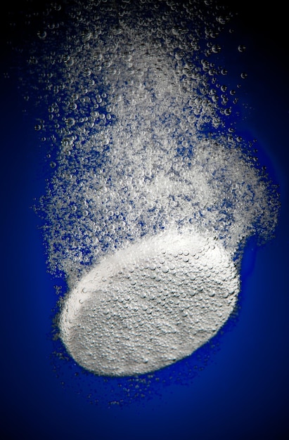 Tableta efervescente en agua con burbujas sobre un fondo azul.