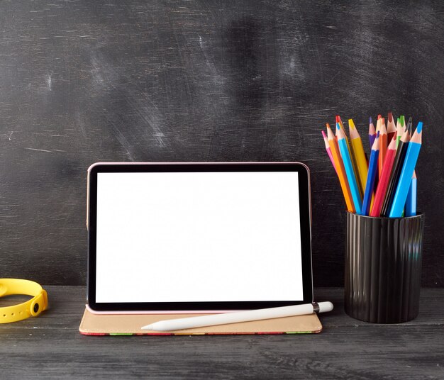 Tableta electrónica con pantalla blanca en blanco y lápices de madera multicolores