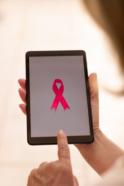 Tableta de explotación de mujer madura con una cinta rosa. Mes de concientización sobre el cáncer de mama con imagen tecnológica.
