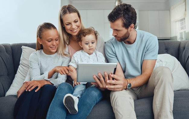 Tableta familiar y en el sofá con los padres hijos o ver dibujos animados para vincular a la madre, el padre y el bebé con la transmisión o la conectividad de las niñas para amar las redes sociales o pasar tiempo de calidad juntos