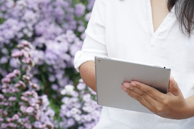 Tableta en manos de una mujer, científico observando plantas de flores púrpuras.