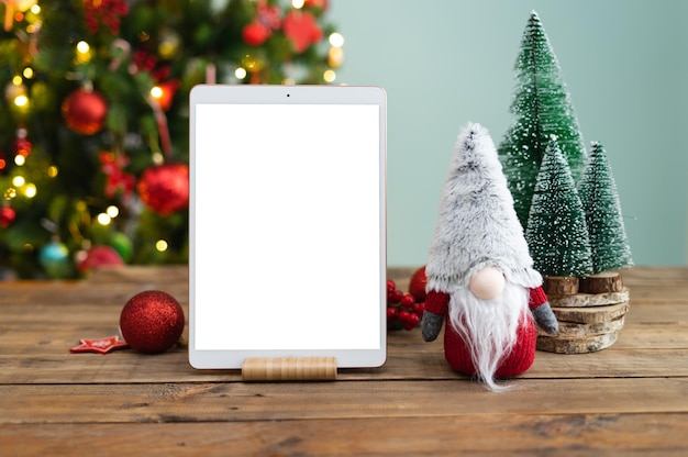 Tableta en mesa de madera con pantalla blanca y decoración navideña con árbol en el fondo archivo Png