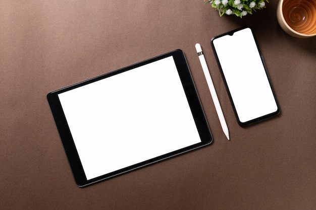 Tableta negra con pantalla blanca en blanco encima de papel marrón con suministros Vista superior plana