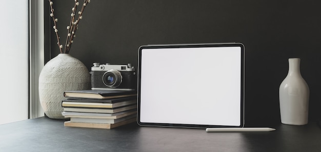 Tableta con pantalla en blanco en un espacio de trabajo oscuro y moderno con suministros de oficina y decoración de jarrones de cerámica