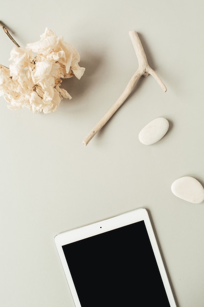 Tableta de pantalla en blanco con piedras, palo y flor de hortensia