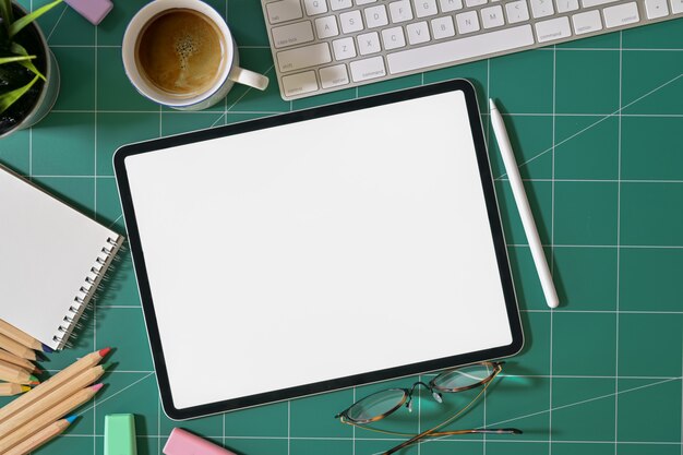 Tableta de pantalla en blanco y suministros de diseñador gráfico en estera de corte verde