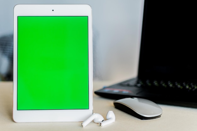 Tableta con pantalla verde junto a una computadora portátil en un escritorio Concepto de tecnología y negocios