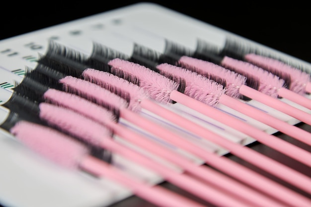 Una tableta con pestañas postizas y pinceles sobre un fondo negro. Accesorios cosméticos para extensiones de pestañas.