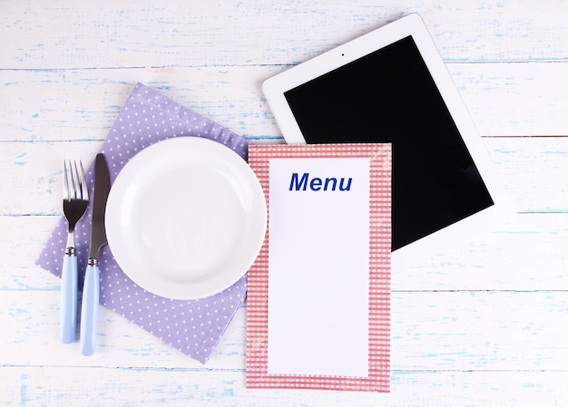 Tableta con plato y cubiertos sobre fondo de madera