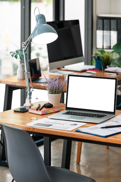 Tableta portátil de pantalla blanca de maqueta con teclado mágico en mesa de madera en espacio de trabajo conjunto.