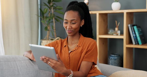 Tableta de saludo y videollamada con una joven negra en una pantalla táctil digital mientras se sienta en el sofá de la sala de estar en casa Videoconferencia de comunicación e Internet con una mujer en las redes sociales