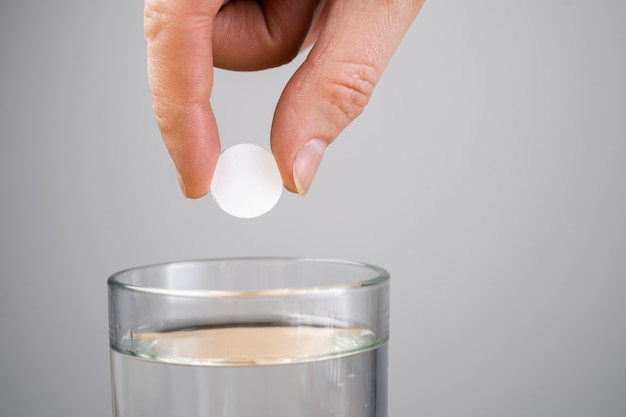 Tableta de sedante en una mano sobre un vaso con agua.