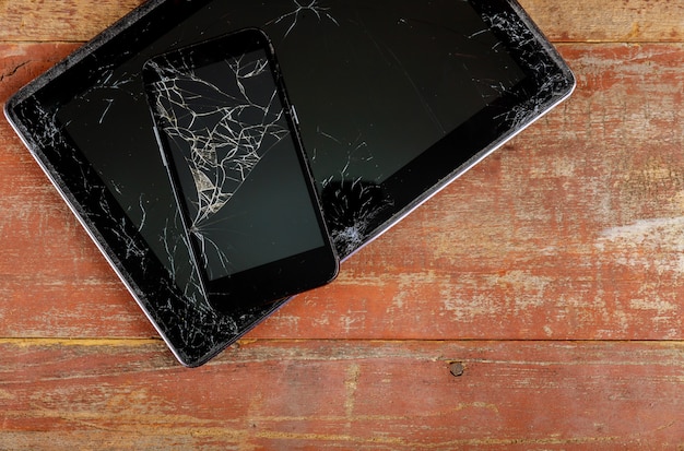 Tableta y teléfono inteligente con pantalla de vidrio roto en el fondo de madera