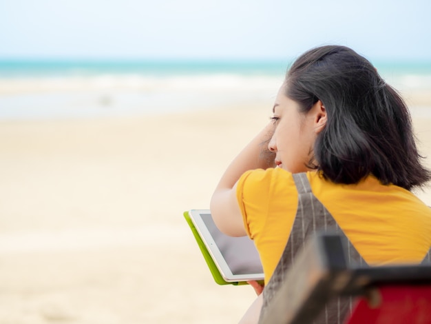 Tableta del uso de la mujer mientras que se relaja en la playa en verano.