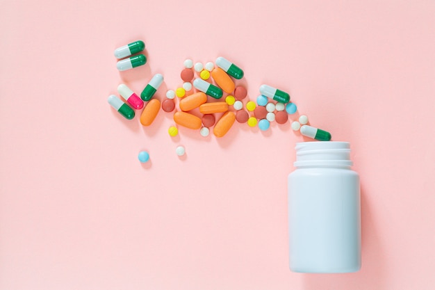 Tabletas multicolores píldoras cápsulas en botella de plástico sobre fondo rosa espacio de copia