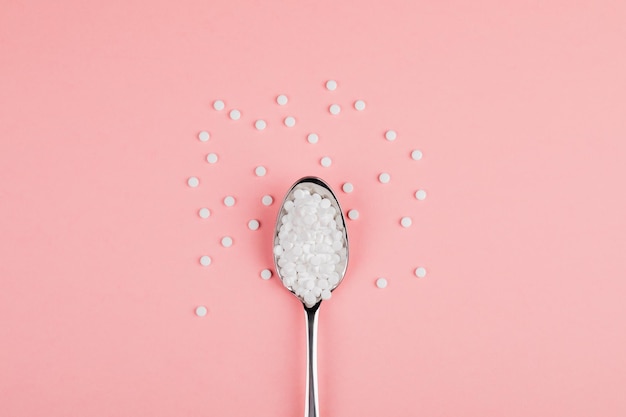Tabletas de reemplazo de azúcar con una cuchara sobre un fondo rosa