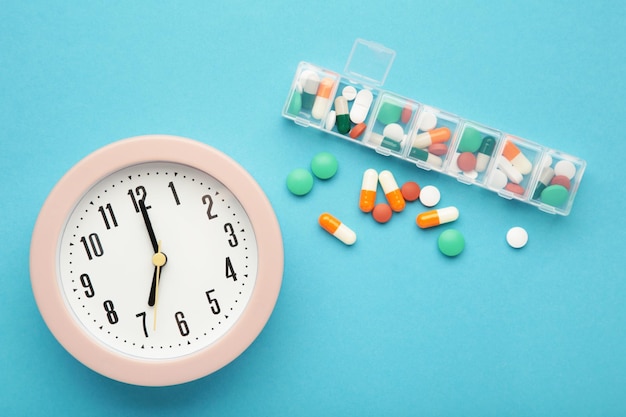 Tabletas de reloj rosa y organizador semanal de tabletas sobre fondo azul Concepto de tiempo de tomar las píldoras
