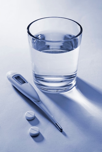 Tabletas, termómetro clínico y vaso de agua.