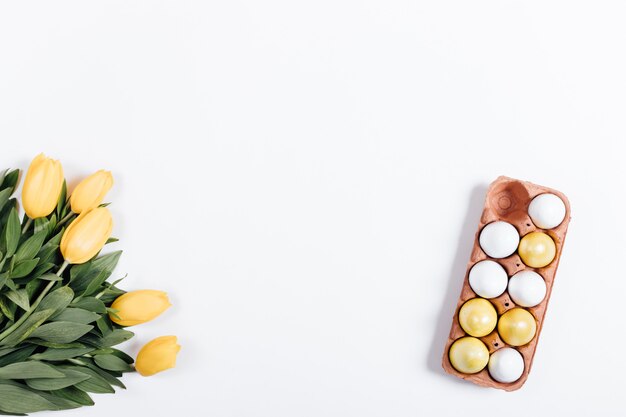 Tablett mit bunten Eiern und gelben Tulpen auf einem weißen Tisch