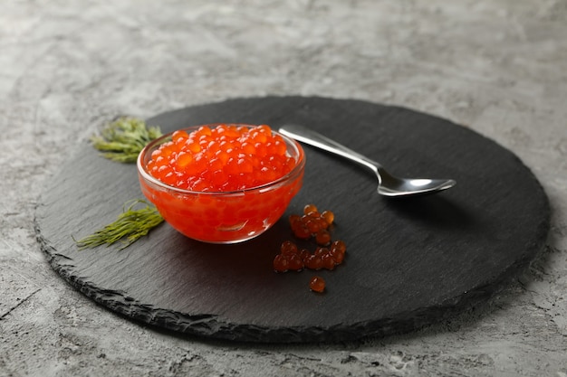 Tablett mit Glas rotem Kaviar, Löffel und Dill auf grauem Hintergrund, Nahaufnahme