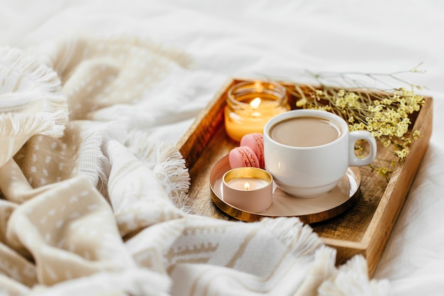 Tablett mit Kaffee und Kerzen mit warmem Plaid auf weißer Bettwäsche. Frühstück im Bett. Skandinavischer Stil. Flache Lage, Ansicht von oben