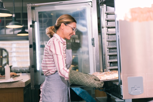 Tablett mit Kuchen. Strahlender Arbeiter der Bäckerei, der Ofen öffnet und Tablett mit erstaunlichem Obstkuchen herausnimmt