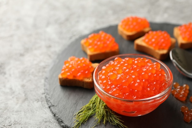 Tablett mit Snacks und Schüssel mit rotem Kaviar auf grauem Hintergrund