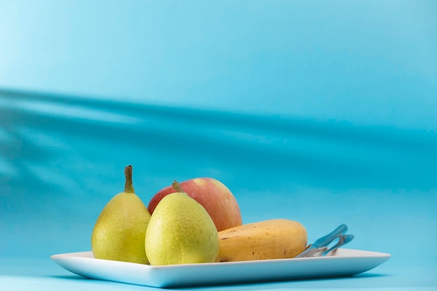 Tablett mit verschiedenen Früchten, Birnen, Apfel und Banane auf blauem Hintergrund