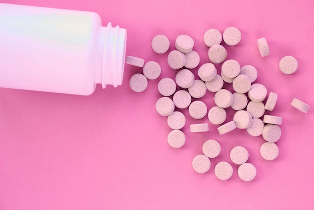 Tabletten, Kapseln, Pillen und weiße Plastikverpackung auf rosafarbenem Hintergrund. Verschreibungspflichtige Vitaminergänzung,