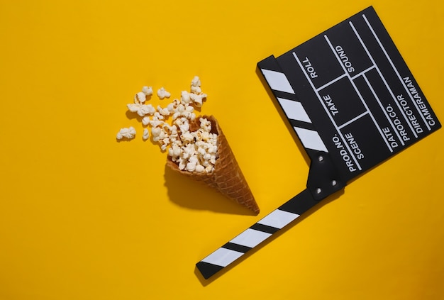 Tablilla de película, cono de galleta de helado con palomitas de maíz sobre fondo amarillo con sombra profunda, vista superior. Tiempo de película. Composición laica plana