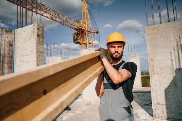 Foto tablón de madera en manos el hombre en uniforme está trabajando en el sitio de construcción