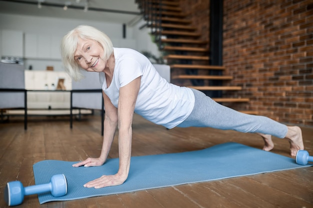 Foto tablón. senior mujer activa en una camiseta blanca haciendo tablón