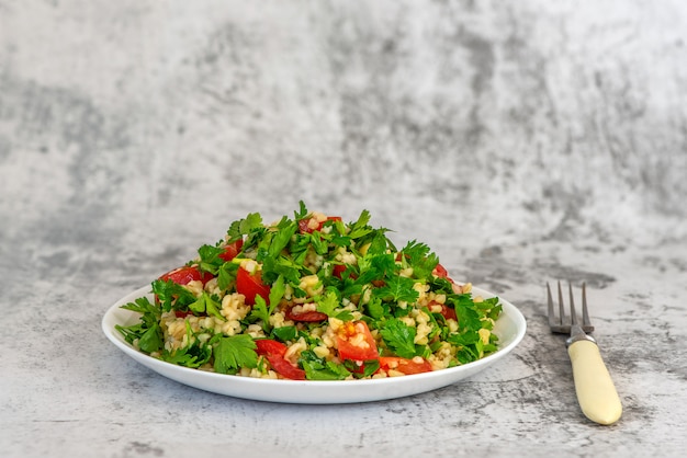 Tabouleh-Salat mit Bulgur, Petersilie, Frühlingszwiebel und Tomate in der Schüssel auf grauem Hintergrund. Draufsicht. Mit Kopierplatz