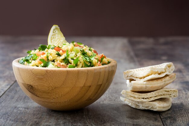 Tabouleh-salat mit couscous- und pittabrot in der hölzernen schüssel auf rustikaler tabelle