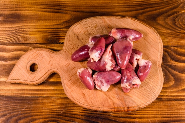 Tábua de cortar com corações de frango cru na mesa de madeira vista superior