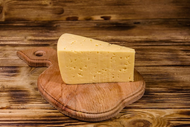 Tábua de cortar com pedaço de queijo na mesa de madeira