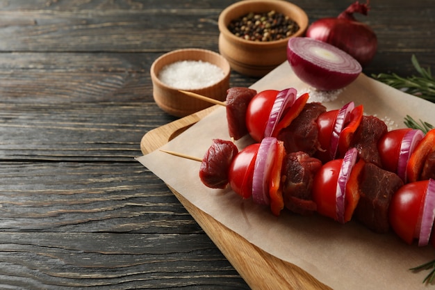 Tábua de cortar com shish kebab cru na mesa de madeira