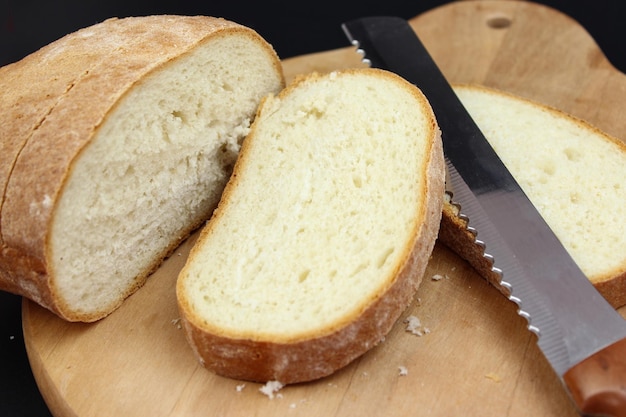 Tábua de corte de madeira com fatias de pão branco e faca em fundo preto