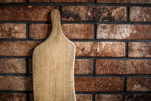 Tábua de corte de madeira na cozinha contra a parede de tijolos