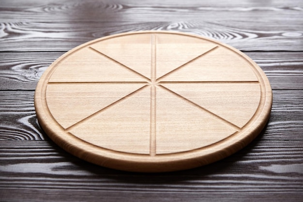 Tábua de corte de pizza redonda com ranhuras de fatia na mesa de madeira marrom